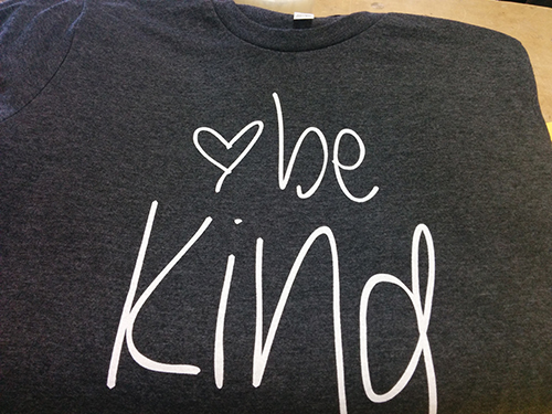 Heather grey custom t-shirt with Be Kind screen-printed on it for clients ordering from the client's custom clothing line.