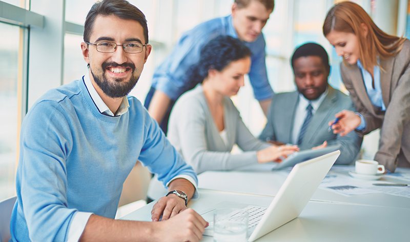 Work employee in a meeting with co-workers wearing blue custom sweater layered with custom shirt.