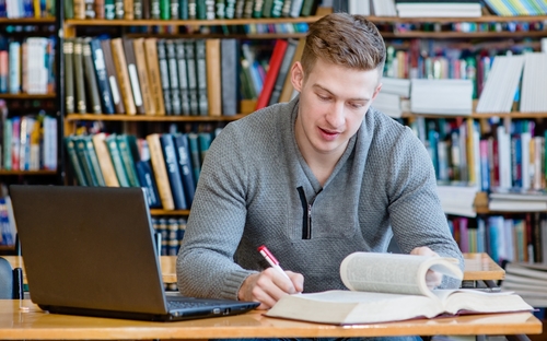 Student-Entrepreneur-in-library-with-laptop-and-books-planning-his-own-business-strategy