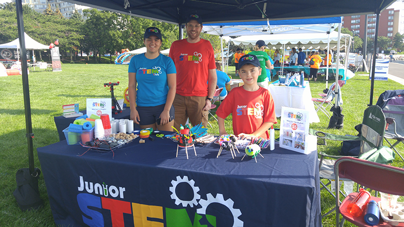 Trade show exhibitors under a tent wearing blue and red custom t-shirt with their company logo.