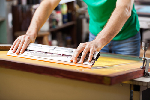 Manually printing custom t-shirt by spreading the paint on the screen.